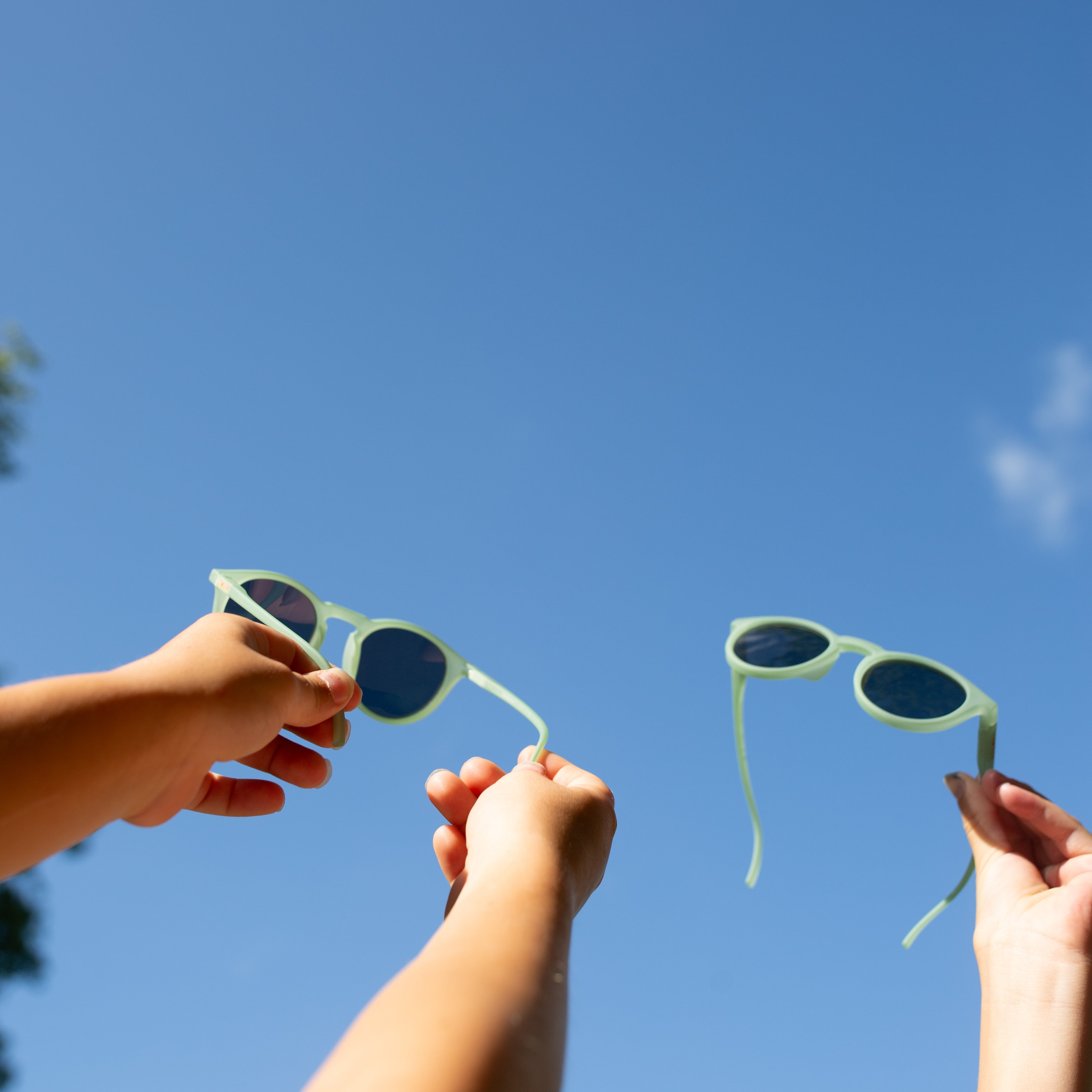 Two pairs of sunglasses held up against a clear blue sky